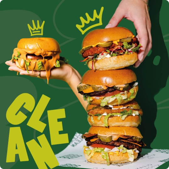 A hand holds a cheeseburger with melting cheese, while another steadies a tall stack of four loaded burgers. Illustrated crowns and the word CLEAN in bold yellow letters pop against the green background, evoking a fun branding case study.